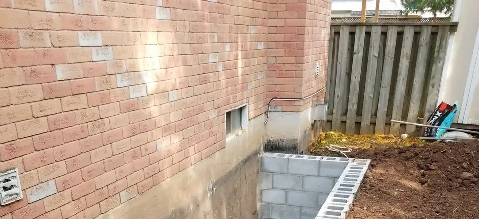 Exterior foundation excavation beside a brick house with new weeping tile and drainage stone